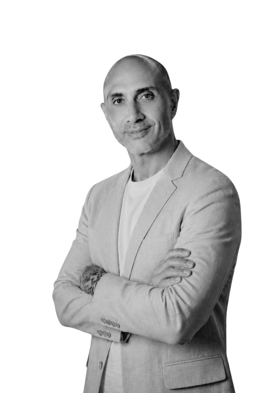 Hisham Abdou, media specialist at Vertical Cuts, standing with arms crossed in a blazer - black-and-white portrait.